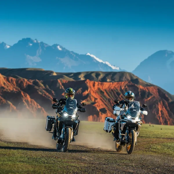 700mt feature 4 Two motorcyclists ride 700MT adventure bikes on a dirt path through a scenic landscape with mountains and red rock formations in the background.
