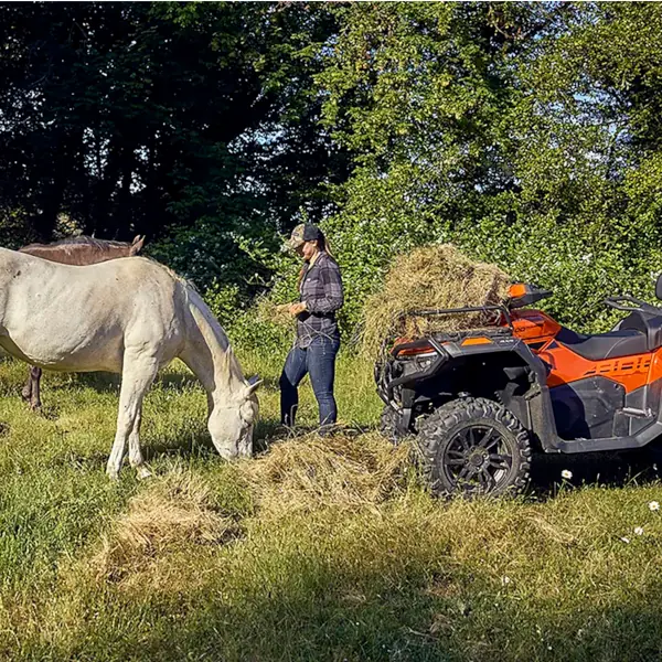 cforce atv horse feeding An equestrian stands near a white horse eating hay beside an orange ATV loaded with hay in a grassy field with trees in the background.
