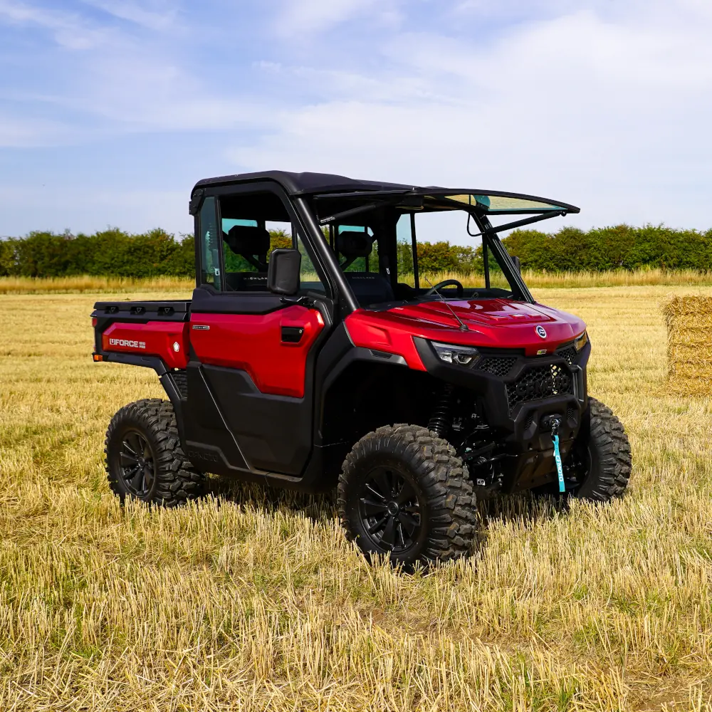 DSC08723 A red UFORCE U10 PRO HIGHLAND off-road utility vehicle is parked on a dry grassy field with hay bales and trees in the background under a partly cloudy sky.