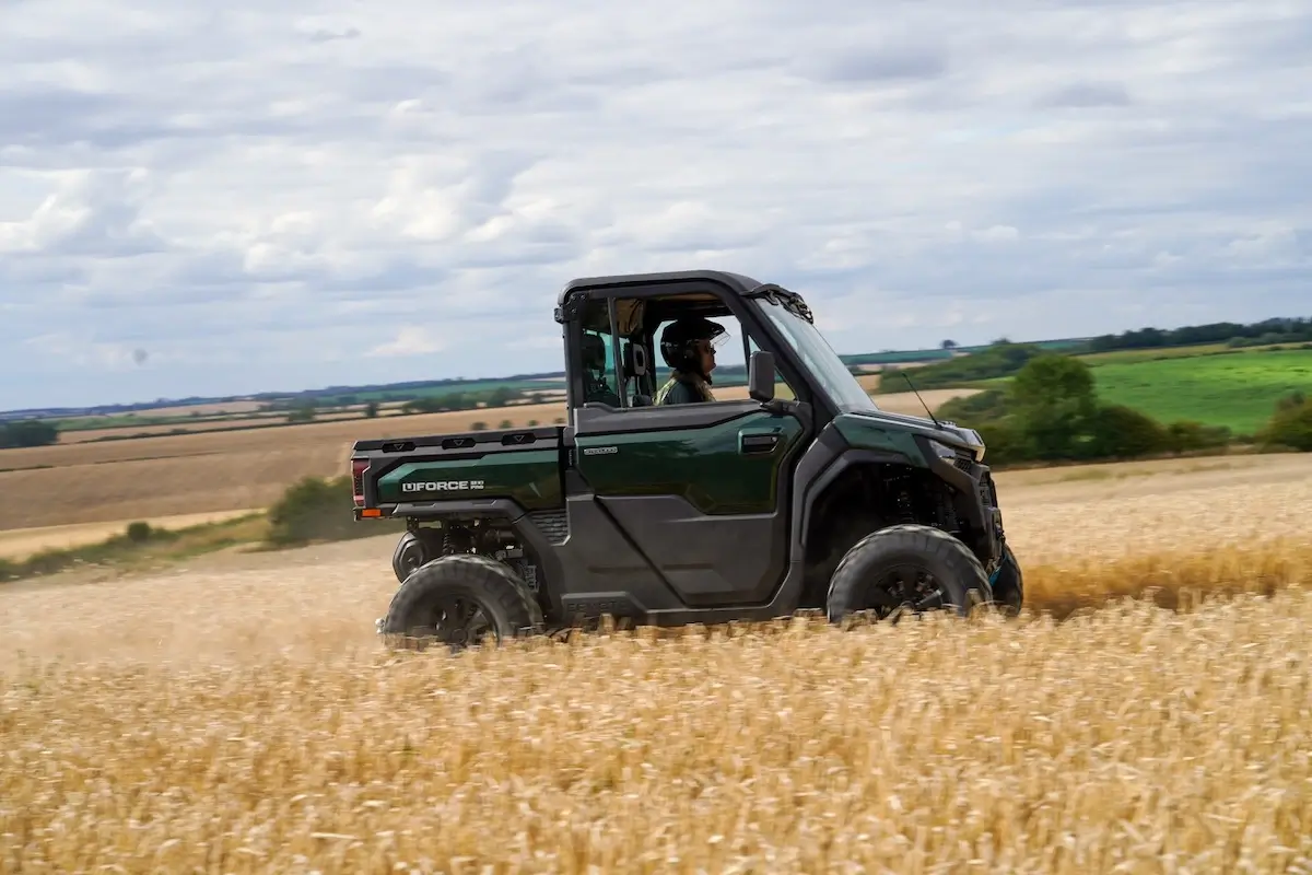 A green UFORCE U10 PRO HIGHLAND off-road utility vehicle drives through a field of tall, golden crops under a partly cloudy sky.