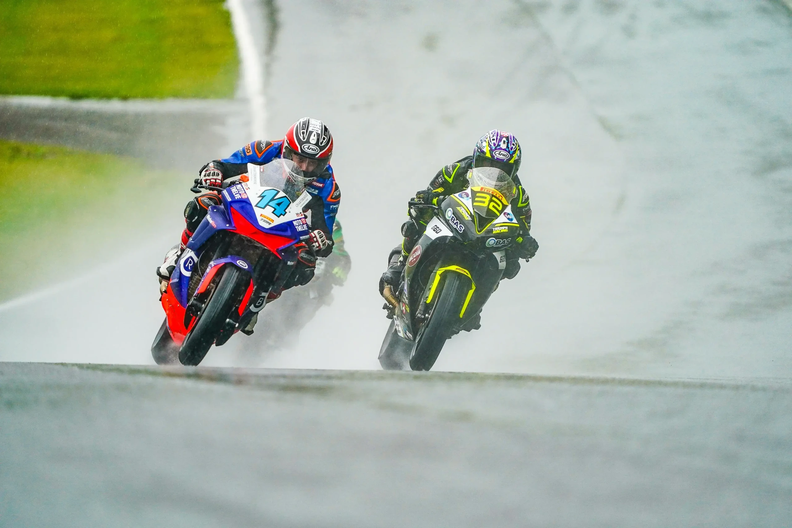 Two motorcycle racers speed around a wet track in rainy conditions during the National Sportbike Championship, leaning into the curve with water spraying from their tires.