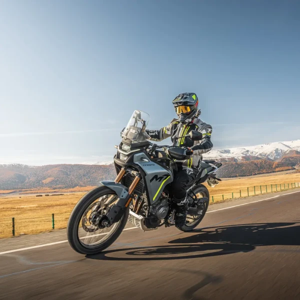 450MT_Outdoor pictures_Others (14) A person wearing full motorcycle gear enjoys leisure riding on an adventure motorcycle along a paved road, surrounded by scenic mountains and open fields.