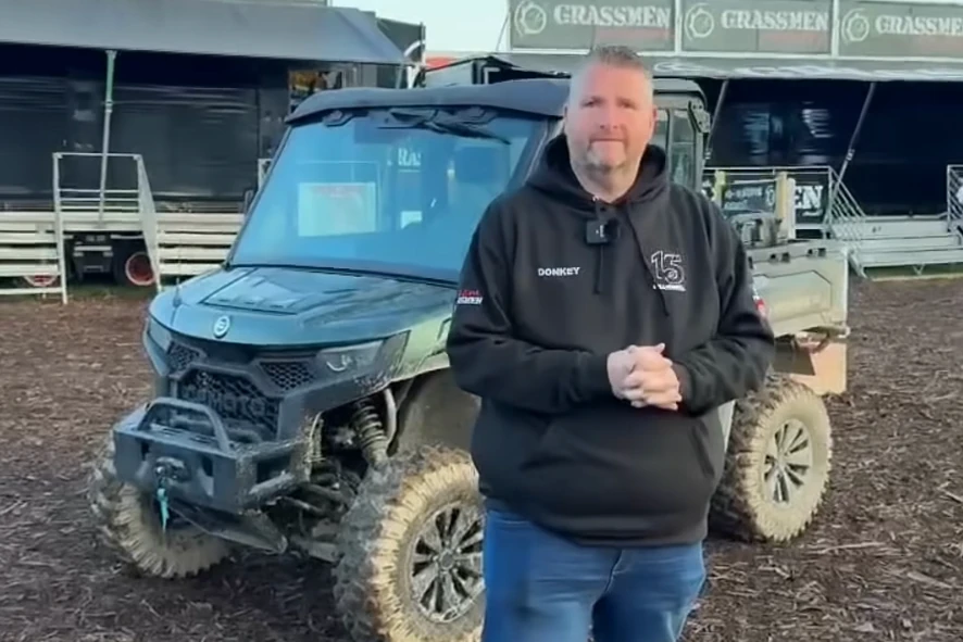 A man stands in front of a muddy UFORCE U10 PRO off-road utility vehicle on a dirt surface, with trailers and "Grassmen" signs visible in the background.