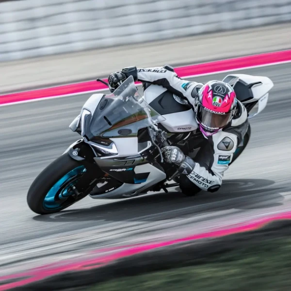 A motorcyclist in full gear leans into a turn on a race track during a track day, riding a white and blue racing motorcycle.