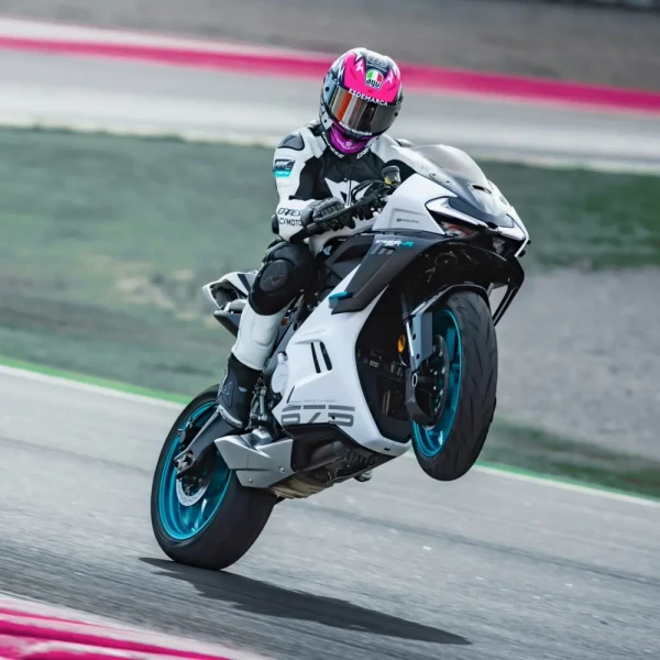 A motorcyclist in full gear performs a wheelie on a white and blue racing motorcycle during an exhilarating track day.