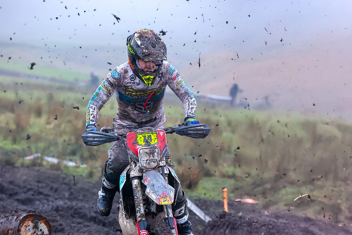 A motocross rider, covered in mud, rides through a muddy track with dirt and debris flying in the air on a foggy day, showing the rugged performance and lasting CFMOTO second-hand value.