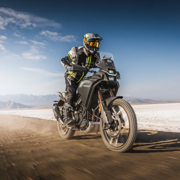Best A2 Motorbikes UK A motorcyclist wearing protective gear rides an A2 motorbike on a dirt road in a desert landscape under a clear blue sky.