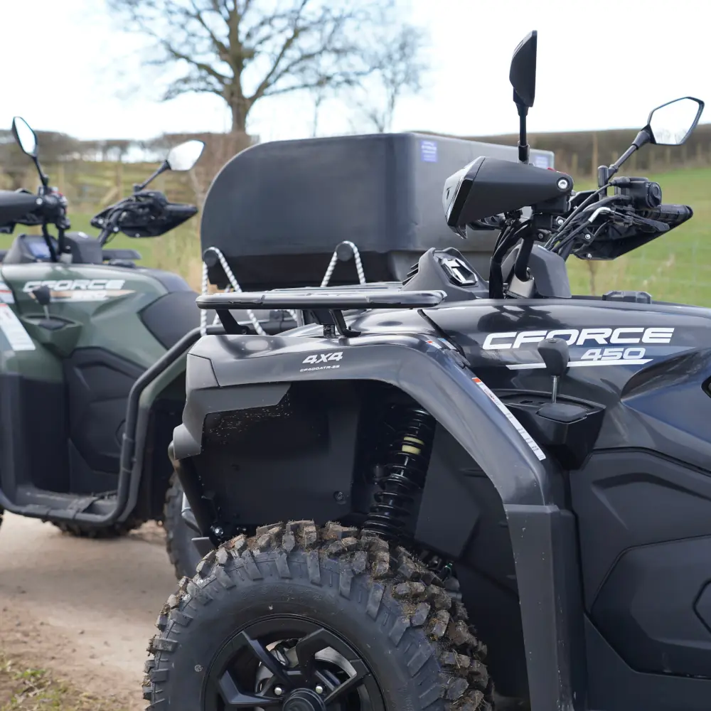 fleet quad bikes Two CFMOTO CFORCE 450 ATVs from the fleet are parked on a dirt track, with one in the foreground and the other partially visible behind it; a tree and field are in the background.