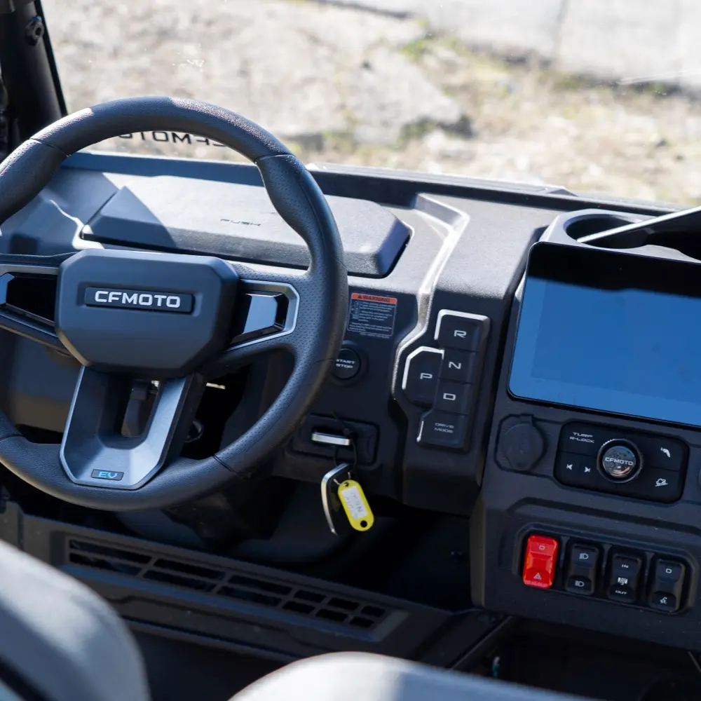 Holiday park utility vehicles Close-up view of a CFMOTO holiday park utility vehicle dashboard showing the steering wheel, gear selector, digital display, control buttons, and a key in the ignition.