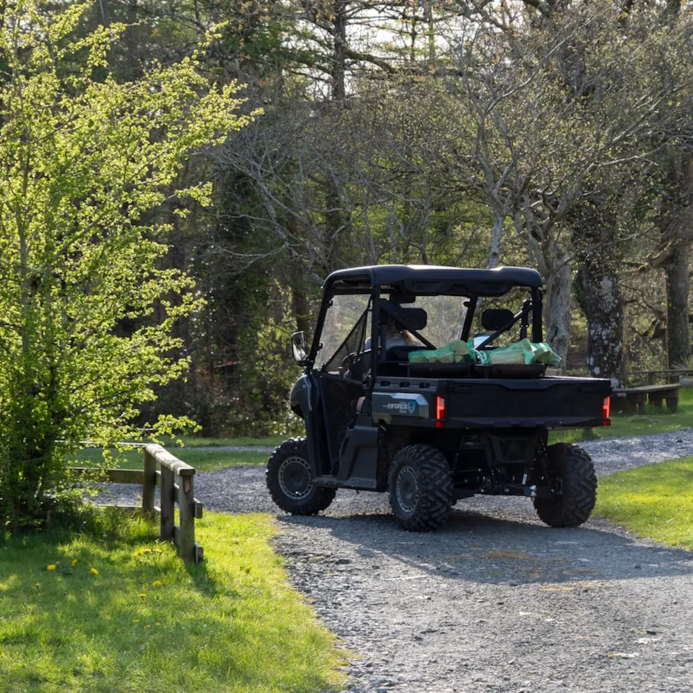 Holiday park utility vehicles A black holiday park utility vehicle drives on a gravel path through a grassy, wooded area on a sunny day.