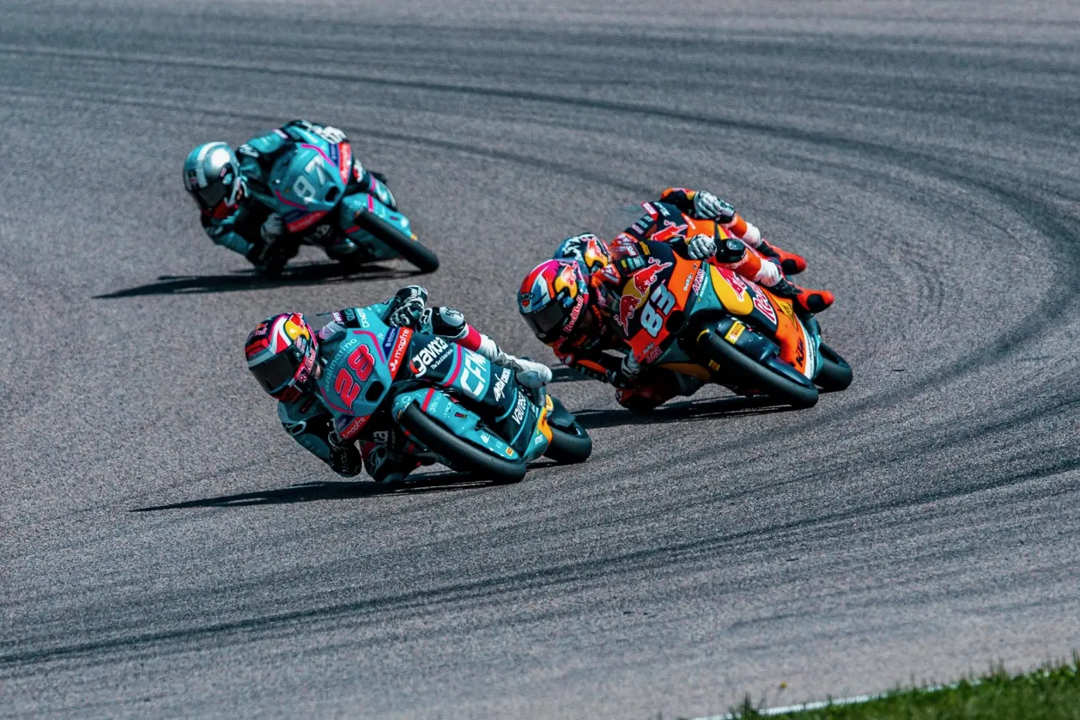 Three motorcycle racers lean into a bend on a Grand Prix racetrack, closely competing while wearing helmets and brightly coloured racing suits, evoking the thrilling energy of the Dutch MotoGP.