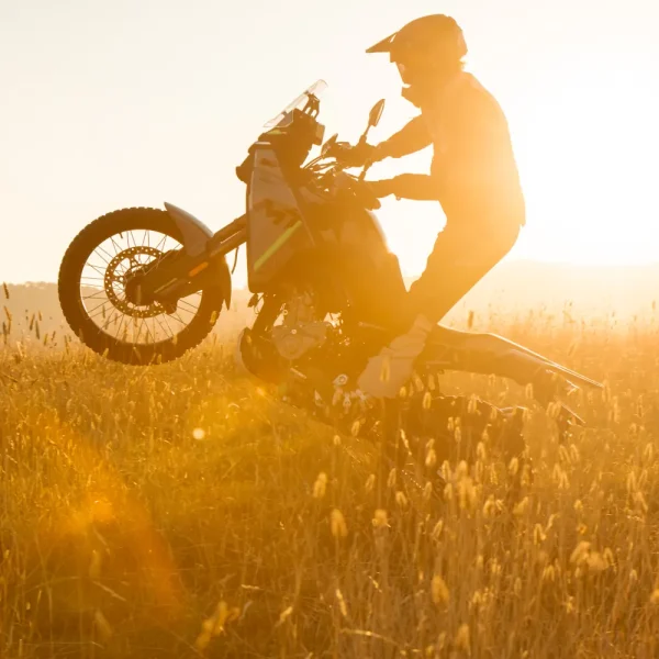 450mt a2 motorbike A person wearing a helmet and kit rides an A2 motorbike, lifting the front wheel, in a sunlit grassy field.
